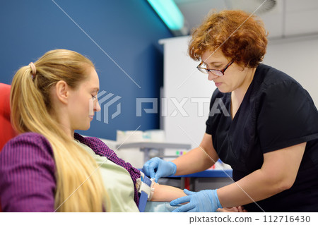 A nurse taking a blood from a young woman for examination in a modern laboratory or hospital. Young adult girl donor is at the time of donation 112716430