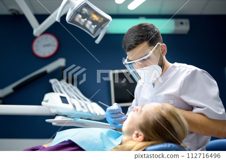 Dentist and patient at modern medical center. Doctor treats a young woman teeth in hospital. Practitioner examines the patient before orthodontists or prosthetics treatment. 112716496