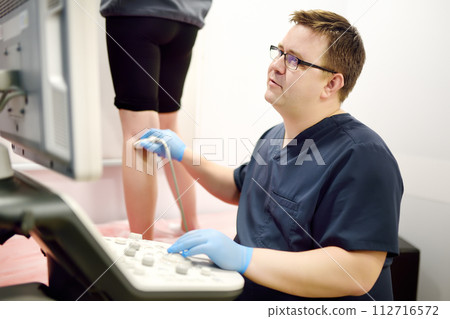 Professional vascular surgeon making ultrasound of the vein of patient in clinic before vein surgery. Phlebectomy Professional vascular surgeon making ultrasound of the vein of patient in clinic before vein surgery. Phlebectomy 112716572