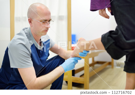 Orthopedic insoles. Fitting orthotic insoles. Flatfoot treatment. Podiatry clinic. Male orthopedist tries insole on patient's foot in clinic. 112716702