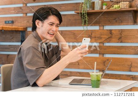 年輕的亞洲男子在咖啡館使用智慧型手機和電腦(驚訝、投資、失敗、麻煩、震驚) 年輕的亞洲男子在咖啡館使用智慧型手機和電腦(驚訝、投資、失敗、麻煩、震驚) 112717281