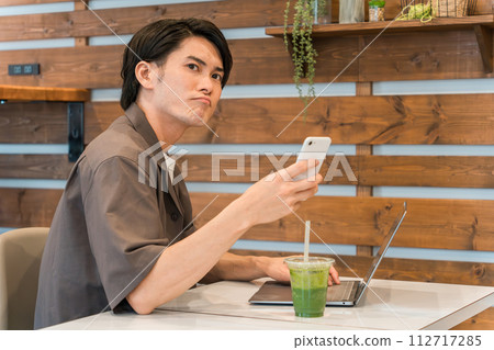 一名年輕的亞洲男子在咖啡館使用智慧型手機和電腦（開會、心情不好、遲到、遲到） 112717285