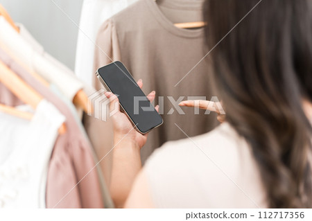 一位女性顧客在服飾店/雜貨店一邊看智慧型手機一邊購物 112717356