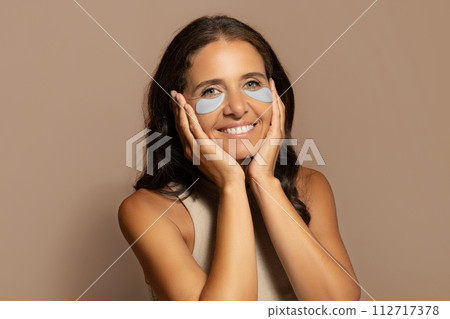 Glad caucasian senior woman put patches under eyes, enjoy skin care, treatment Glad caucasian senior woman put patches under eyes, enjoy skin care, treatment 112717378