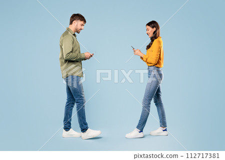 Man and woman in casual wear, using smartphones, walking to each other 112717381