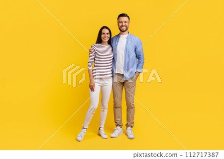 Portrait of smiling caucasian couple in casual clothes standing against yellow background 112717387