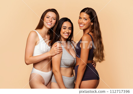 Three cheerful multiracial women in underwear embrace and smile 112717396