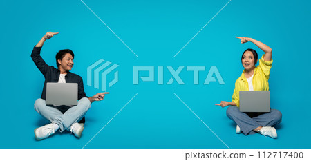 Excited man and woman sitting with laptops, pointing to empty space ideal for advertising content Excited man and woman sitting with laptops, pointing to empty space ideal for advertising content 112717400