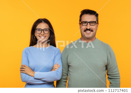 Happy european old couple in glasses, smiling and confidently standing with arms crossed Happy european old couple in glasses, smiling and confidently standing with arms crossed 112717401