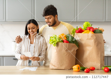 Happy indian couple with bag full of food checking bill Happy indian couple with bag full of food checking bill 112717447
