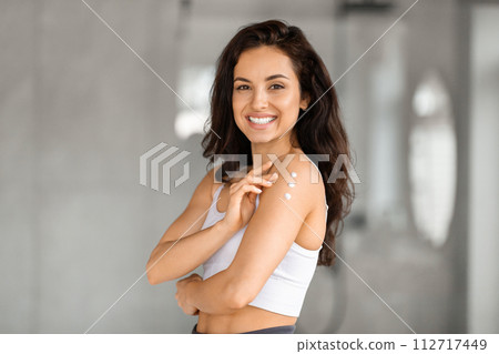 Smiling attractive brunette woman applying body lotion Smiling attractive brunette woman applying body lotion 112717449