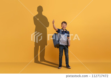 A young boy with a backpack gives a thumbs up in front of a yellow background A young boy with a backpack gives a thumbs up in front of a yellow background 112717472