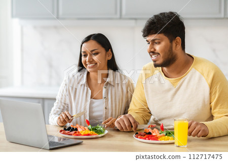 Cheerful indian couple have breakfast and watching movie on laptop Cheerful indian couple have breakfast and watching movie on laptop 112717475
