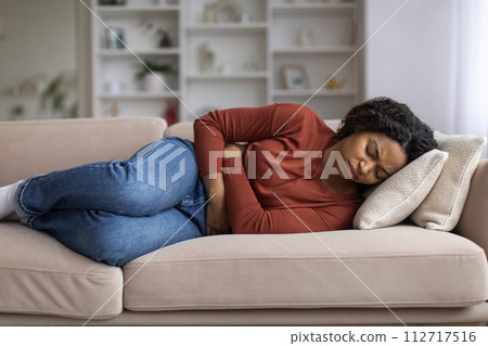 Young black woman clutching her abdomen in discomfort at home Young black woman clutching her abdomen in discomfort at home 112717516