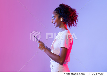 Happy black lady with smartphone and earbuds on pink and purple background 112717585