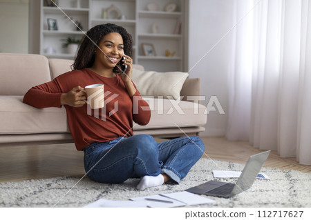 Black Woman Talking On Cellphone And Drinking Coffee While Working With Laptop 112717627