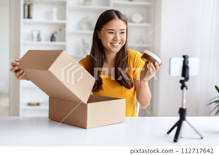 Cheerful asian vlogger presenting new cosmetic product from an open box 112717642