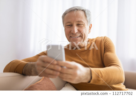 Older man viewing smartphone with pleasant smile 112717702