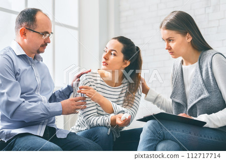 Concerned support group mebers comforting emotional young woman at therapy session 112717714