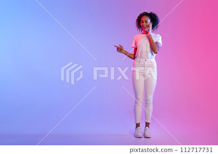 Smiling black lady pointing to side at free space on blue and pink gradient background 112717731