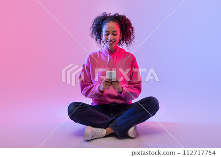 Smiling black lady using smartphone on neon background 112717754