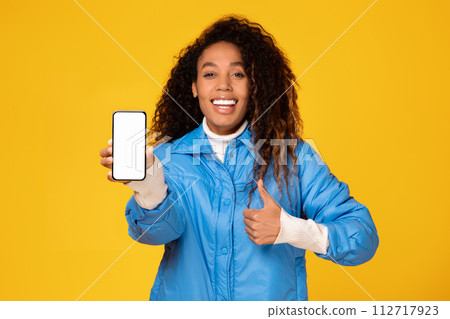 Black lady in jacket showing phone with blank screen gives thumbs up 112717923