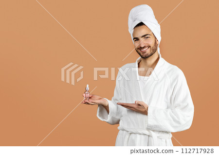 Hispanic young man shows facial serum product against beige backdrop 112717928