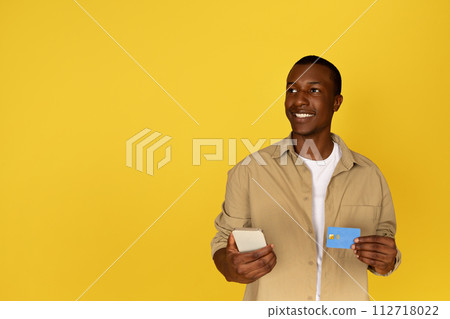 Cheerful pensive young black man use mobile phone and credit card Cheerful pensive young black man use mobile phone and credit card 112718022