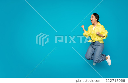 Excited young woman in mid-air jump with a fist pump, wearing a bright yellow blouse 112718066