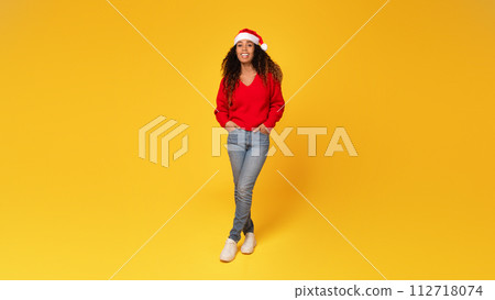 Joyful young black lady in Santa hat posing on yellow background, full length 112718074