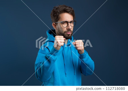 Determined man wearing eyeglasses and hoodie raising his fists in defensive pose 112718080