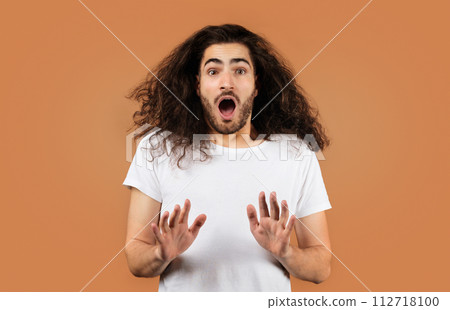 Shocked guy with curly hair showing stop gesture, beige backdrop 112718100