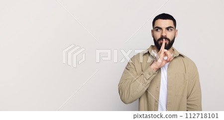 Serious handsome young middle eastern man with beard in casual make shhh gesture with finger lips 112718101