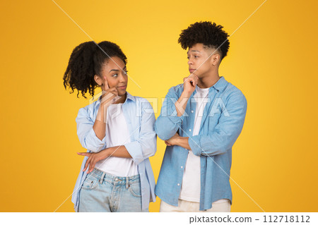 Thoughtful young African American woman and man with hands on chin, looking at each other Thoughtful young African American woman and man with hands on chin, looking at each other 112718112