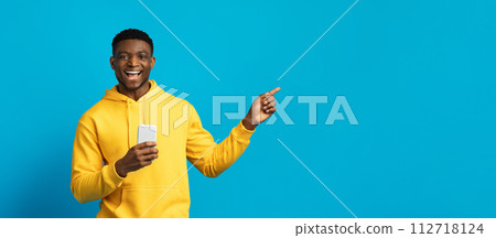 Happy young black guy in yellow hoodie using smartphone, panorama Happy young black guy in yellow hoodie using smartphone, panorama 112718124