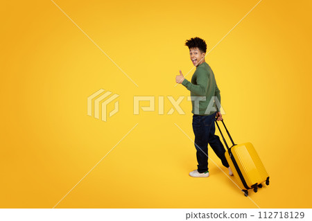 Young black guy tourist with suitcase showing thumb up 112718129