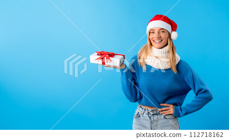 Young woman in Santa hat holding gift, blue background, panorama with free space Young woman in Santa hat holding gift, blue background, panorama with free space 112718162