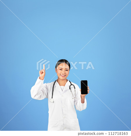 Smiling asian female physician in uniform holding smartphone with empty screen 112718163