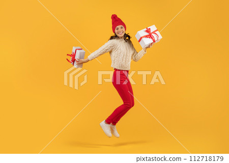 Cheerful young woman jumps with Xmas gift boxes, yellow backdrop Cheerful young woman jumps with Xmas gift boxes, yellow backdrop 112718179