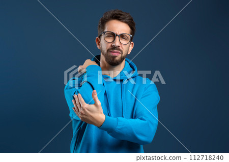 Young upset man clutching his elbow in pain or discomfort, 112718240