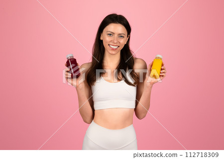 Happy young woman in a white sports top holding two bottles of colorful detox juice Happy young woman in a white sports top holding two bottles of colorful detox juice 112718309