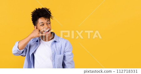 Joyful black guy making call me gesture against yellow background 112718331