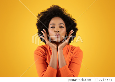 Charming young woman with curly afro hair wearing an orange sweater 112718375