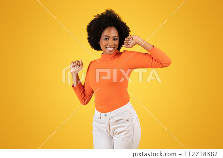 Joyful young African American woman with a playful wink, dancing 112718382