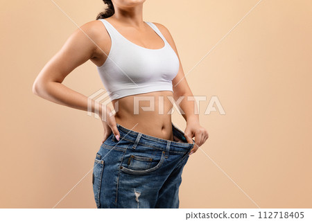 Fit woman confidently demonstrating successful weight loss by pulling out oversized jeans. Fit woman confidently demonstrating successful weight loss by pulling out oversized jeans. 112718405