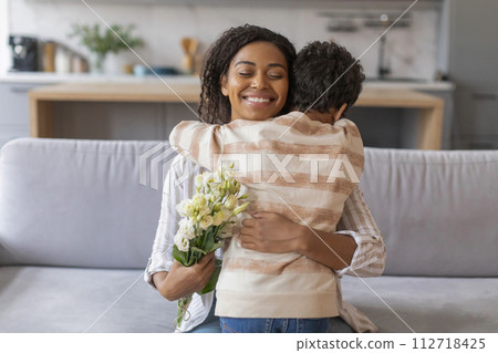 Little black boy giving loving hug and flowers bouquet to happy mother Little black boy giving loving hug and flowers bouquet to happy mother 112718425
