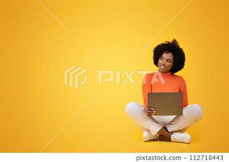 Content young African American woman with curly hair sitting cross-legged holding a laptop Content young African American woman with curly hair sitting cross-legged holding a laptop 112718443