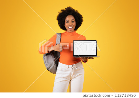 Excited young woman with an afro showcasing a laptop with a blank screen 112718450