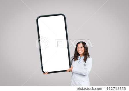 Positive european female doctor displaying huge cellphone with white empty screen, mockup 112718553