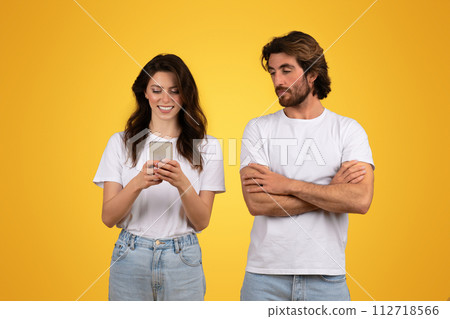 Smiling woman happily engrossed in her smartphone with a curious man beside her Smiling woman happily engrossed in her smartphone with a curious man beside her 112718566